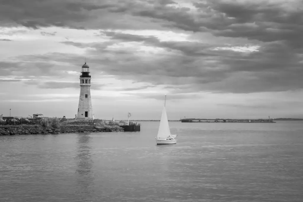 Lighthouse on the shore with a sailboat in the foreground, capturing the serene waterfront of East Aurora, NY, in black and white.