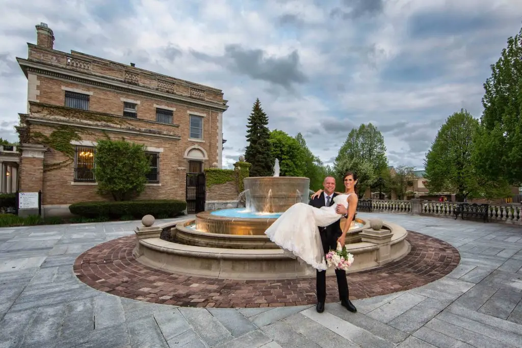 Bride in groom&rsquo;s arms by the fountain at The Mansion on Delaware in Buffalo, NY &ndash; captured by John Angelo Photography