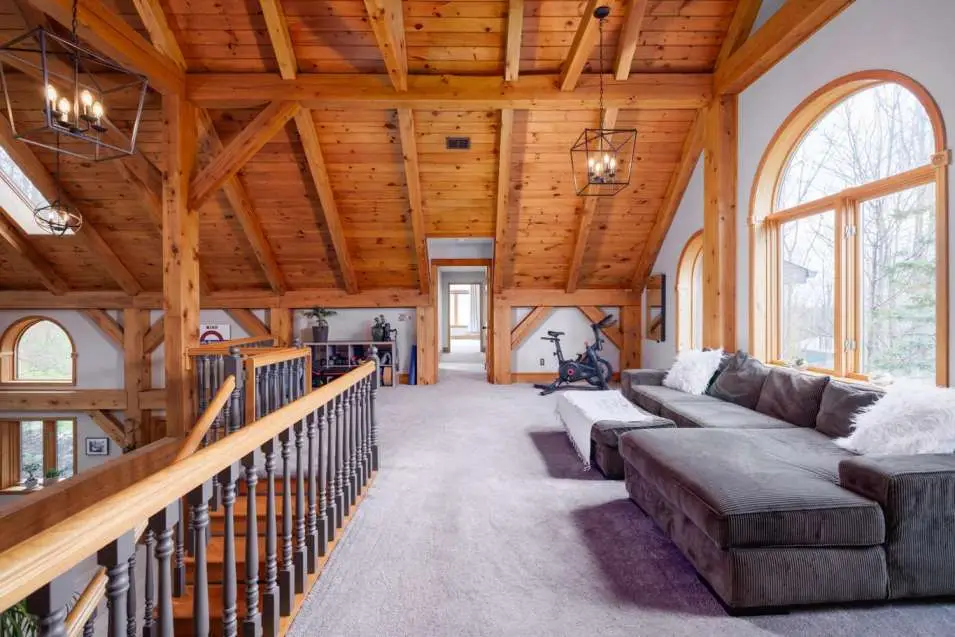 Spacious loft area showcasing exposed wooden beams, large arched windows, and a cozy sectional sofa, emphasizing the blend of rustic charm and modern living in a real estate listing at 930 Underhill Road, East Aurora, NY.